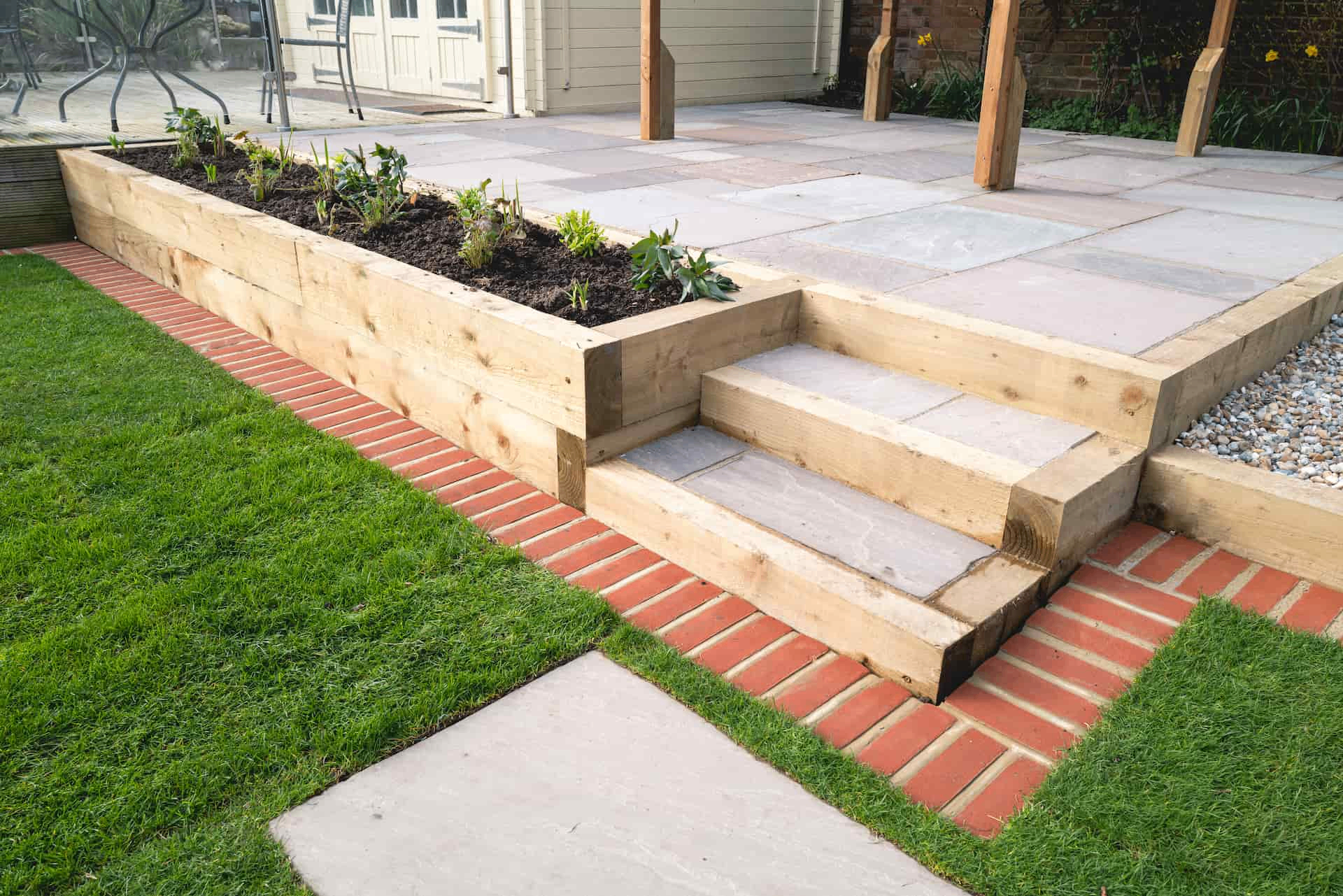 Indian sandstone steps with timber sleeper risers, brick edging and a raised planter beside a lawn