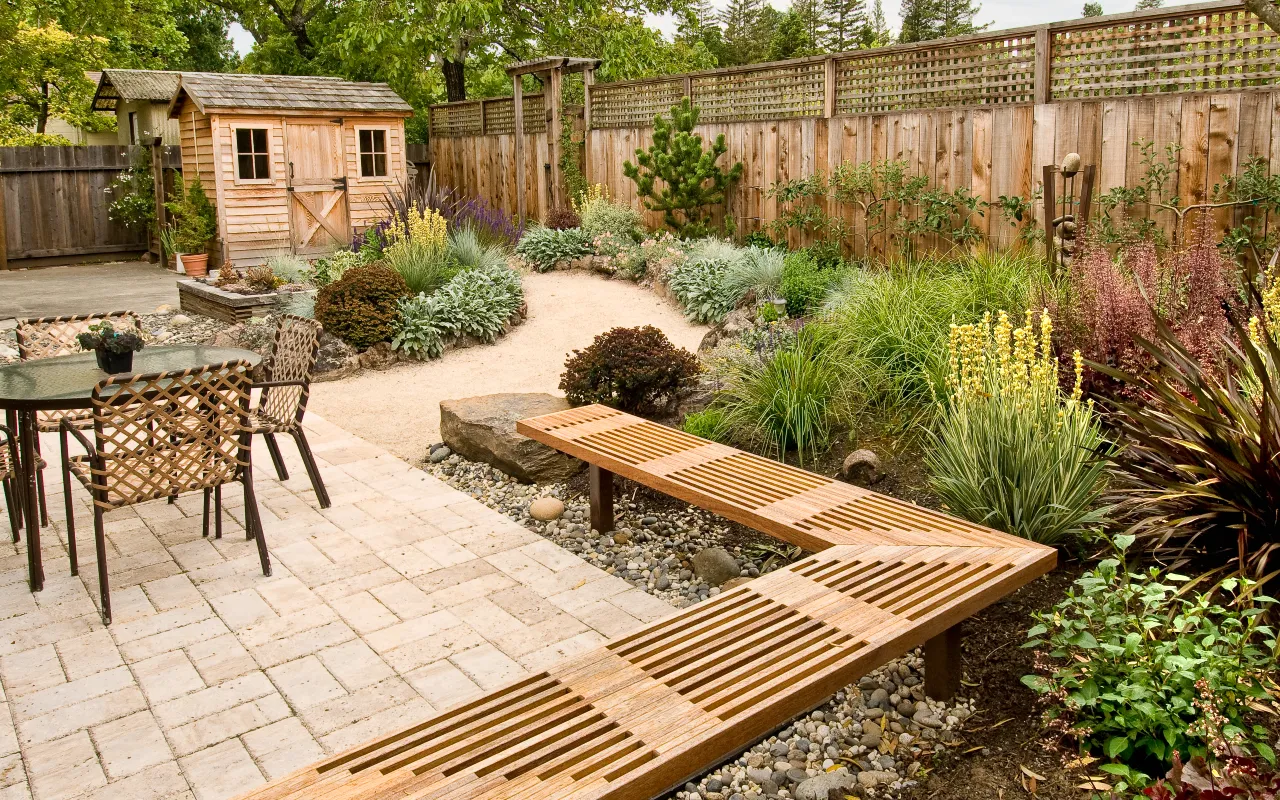 Garden patio with paving, gravel border and a wooden bench leading into the garden